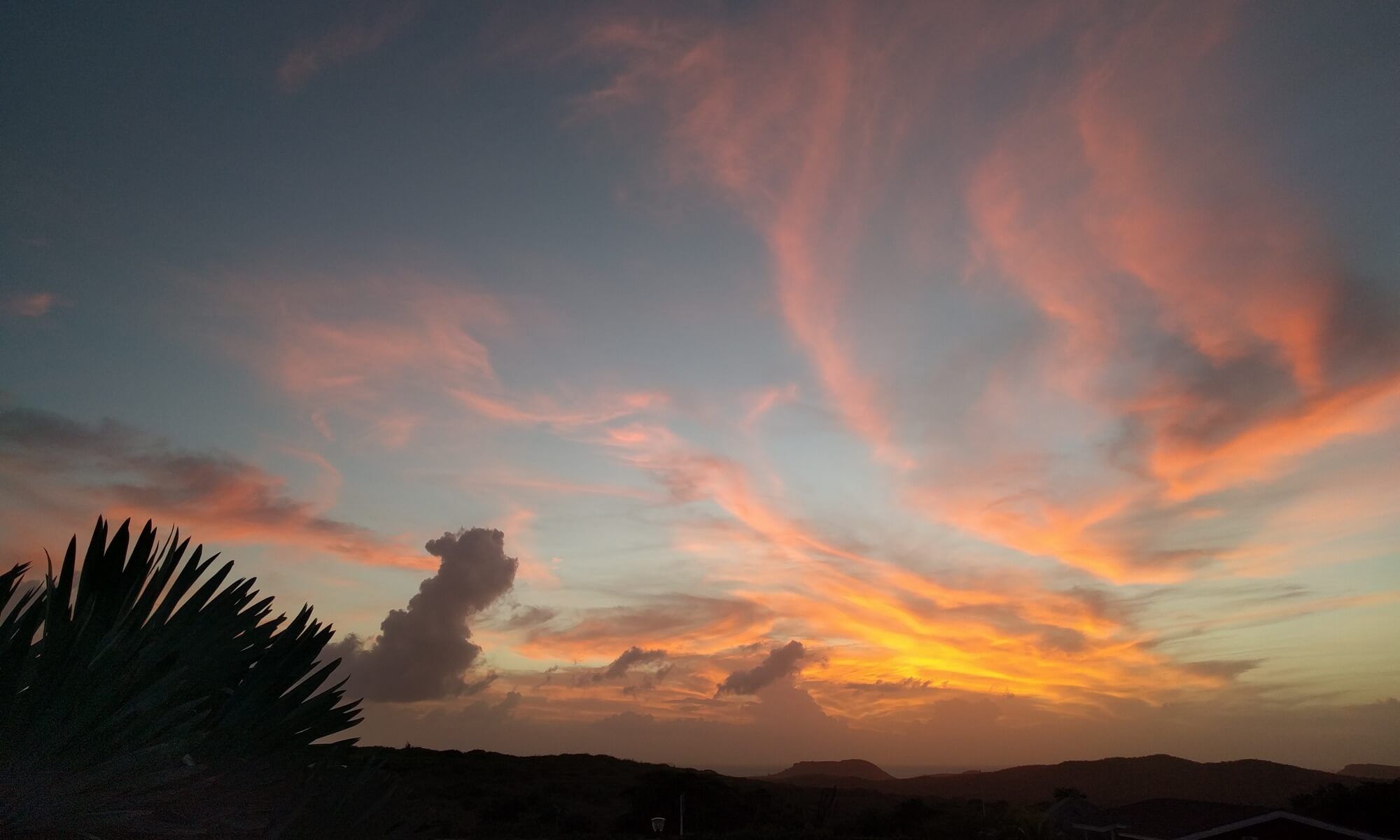 Orange and pink clouds at sunset above the hills, seen from the terrace
