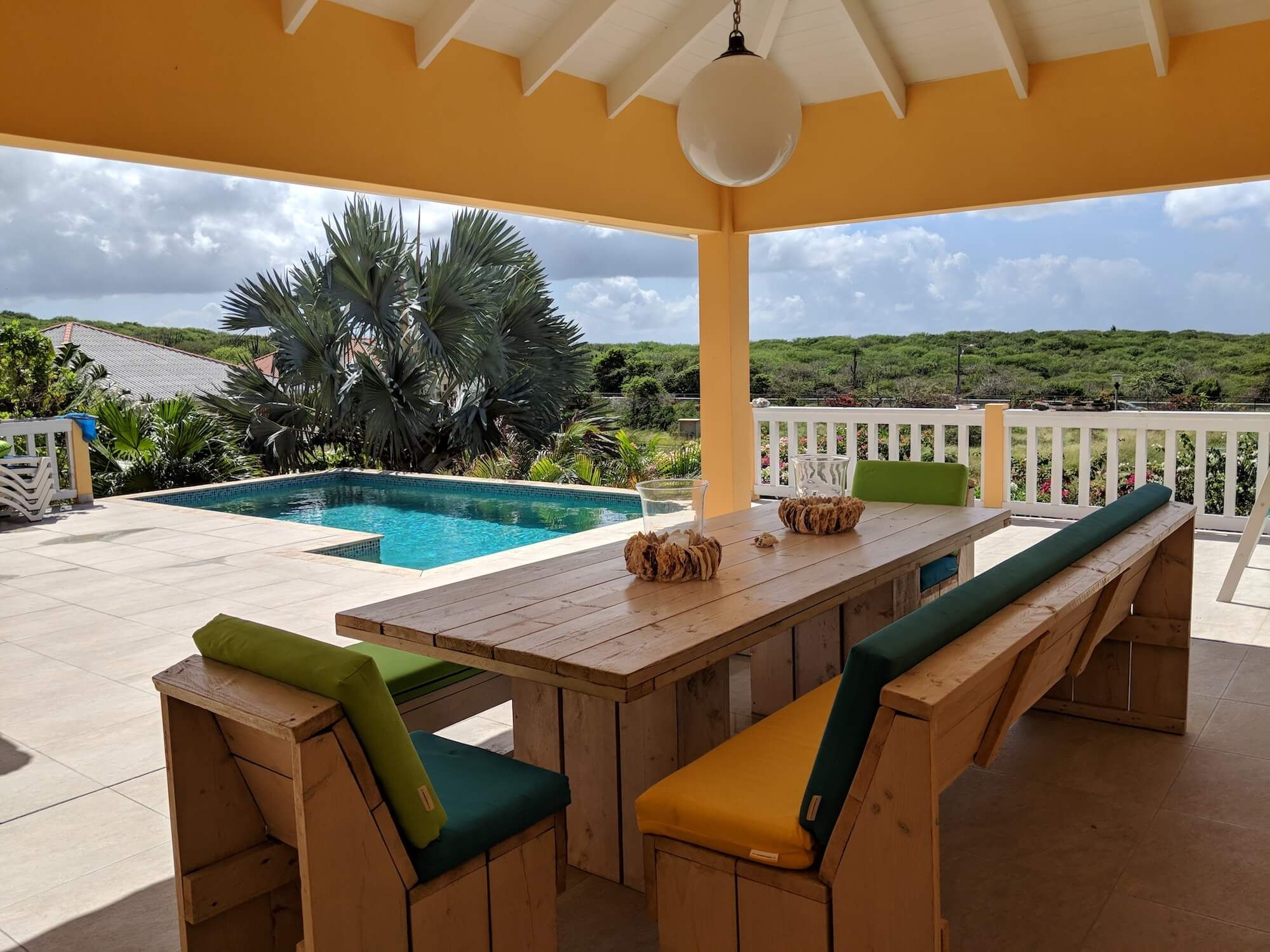 Der große Holz-Esstisch mit Bänken unter der Veranda, mit Blick auf Pool und Hügel