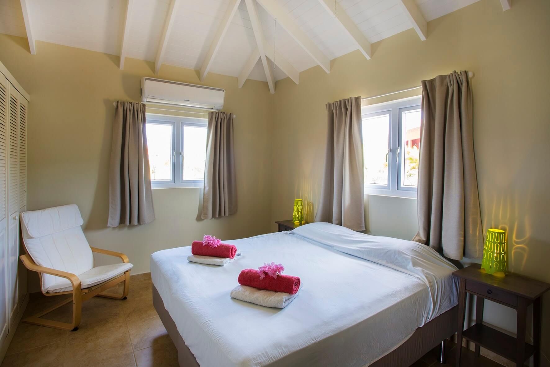 A bedroom with a made-up double bed, armchair and two windows