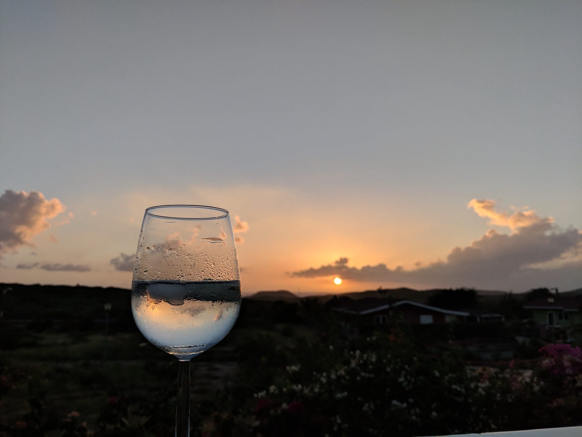 Ein Weinglas auf dem Terrassenrand, dahinter die untergehende Sonne